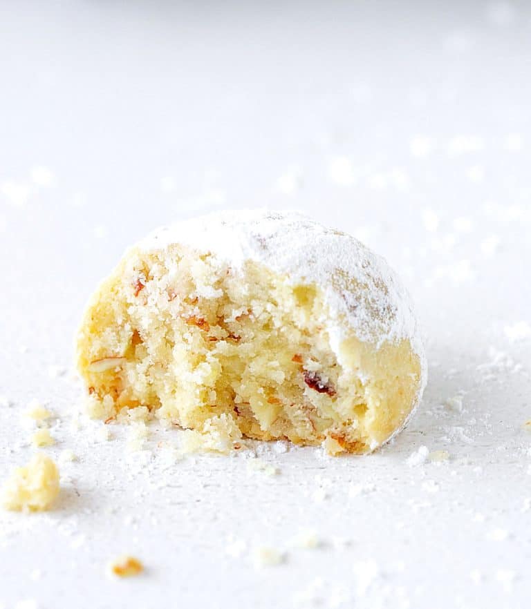 Crumbly round butter cookie, bitten, white surface with crumbs and powdered sugar