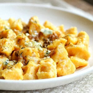 White round plate with pumpkin gnocchi on a white cloth.