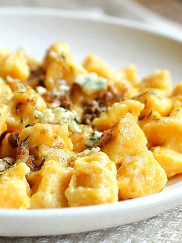 White round plate with pumpkin gnocchi on a white cloth.