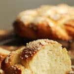Red and white text on image of holiday braid slice and whole bread on grey background