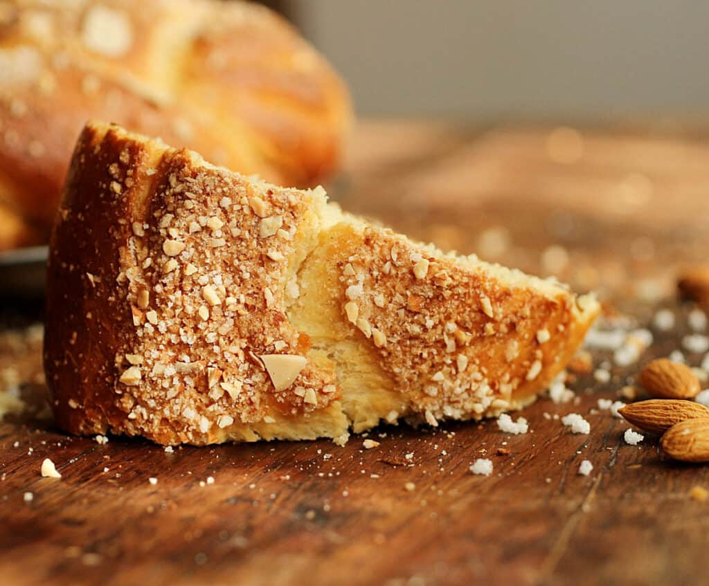 On a wooden table a single piece of crunchy topped holiday bread, pearl sugar and almonds around