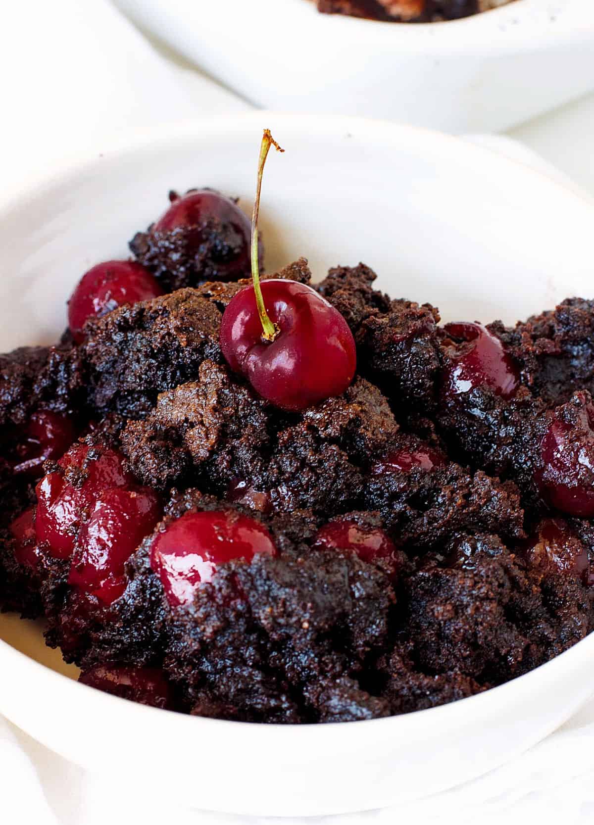 Cherry chocolate dump cake portion in a white bowl on white surface