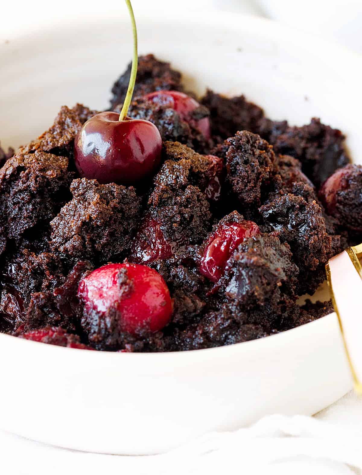 White bowl with chocolate cherry dump cake, a spoon.