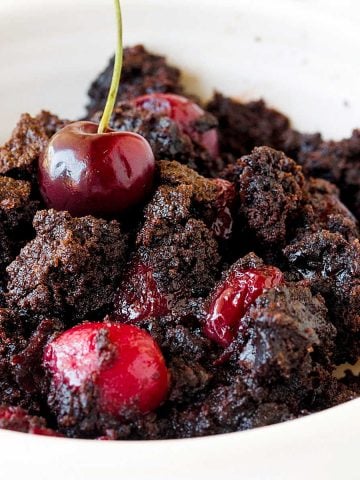 Close up of chocolate cherry dump cake serving in a white bowl.