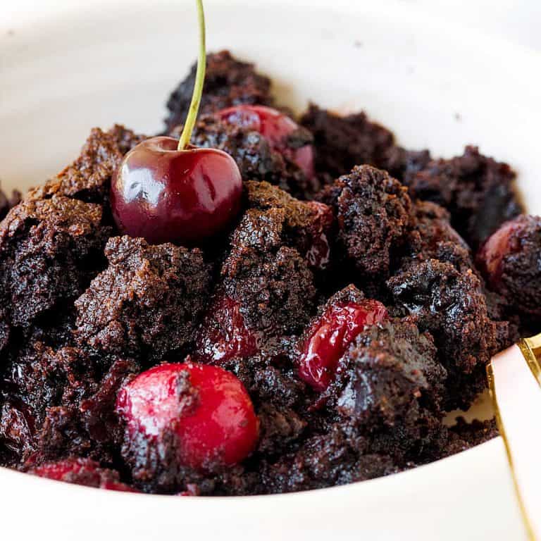 Close up of chocolate cherry dump cake serving in a white bowl.