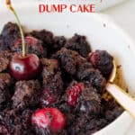 Partial view of white bowl with serving of chocolate cherry dump cake, spoon, white surface