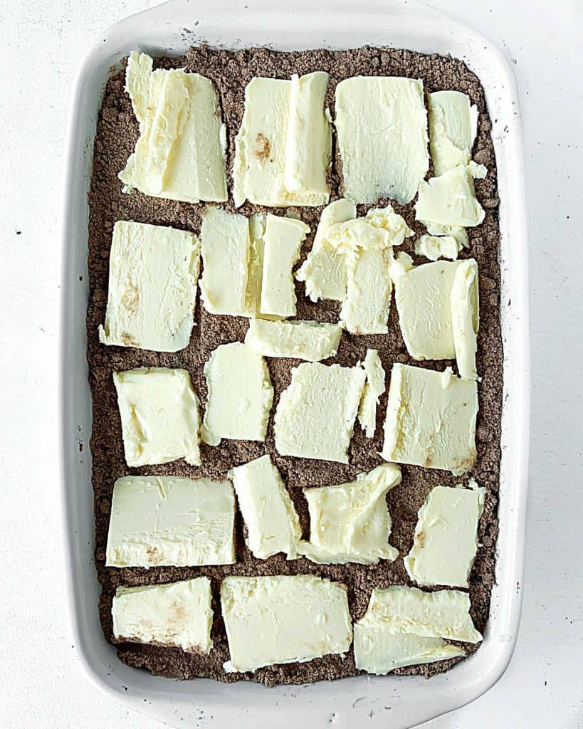 Butter slices over chocolate cake mix in a rectangular white ceramic dish on a white surface.
