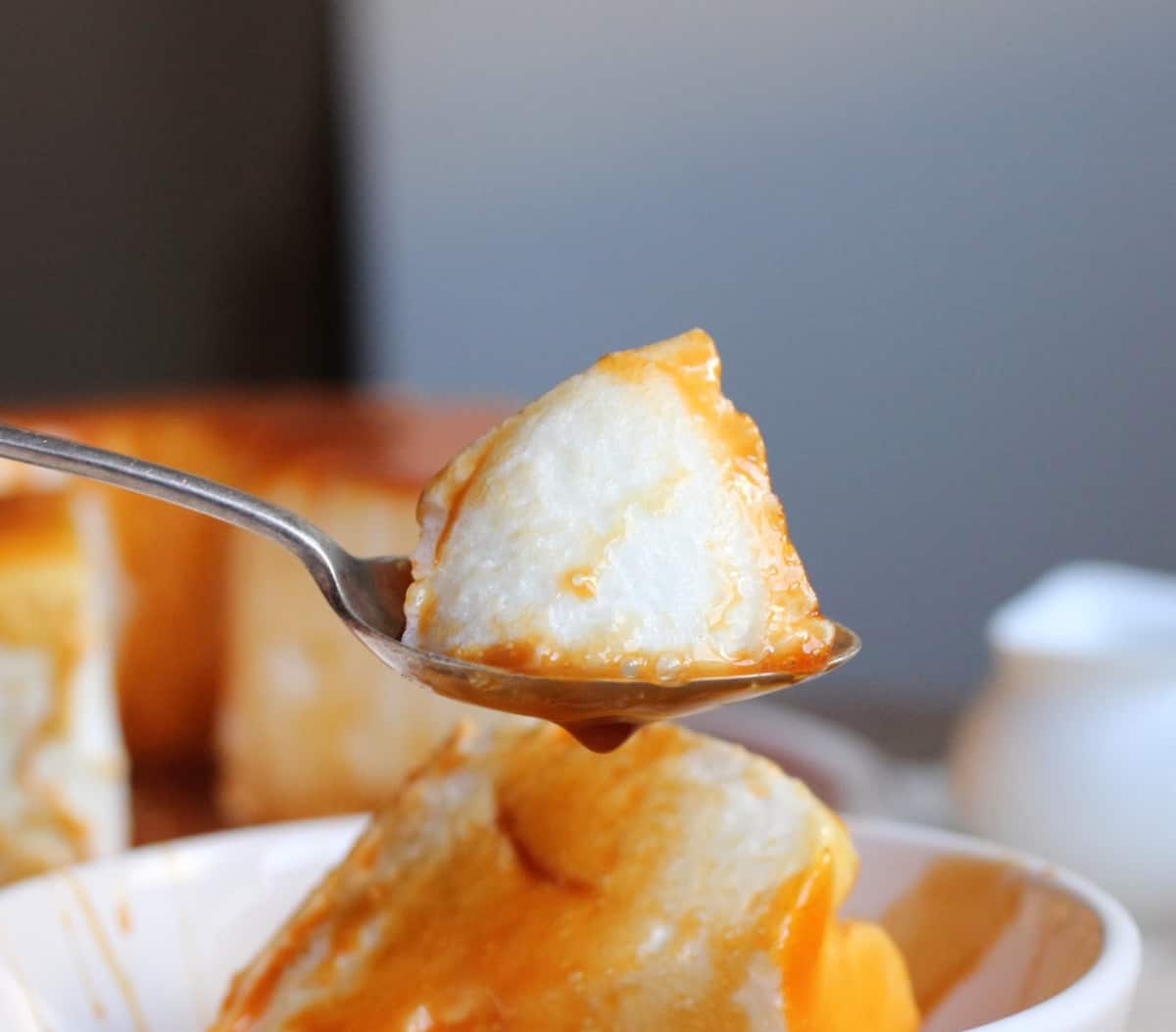 Bite of floating island on metal spoon, grey background with rest of the dessert.