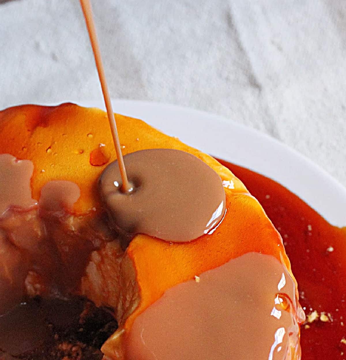 Pouring dulce de leche sauce on caramel floating island dessert; whitish cloth underneath