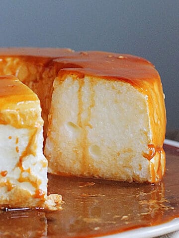 Close up of floating island with a missing slice on a white plate and dulce de leche sauce.