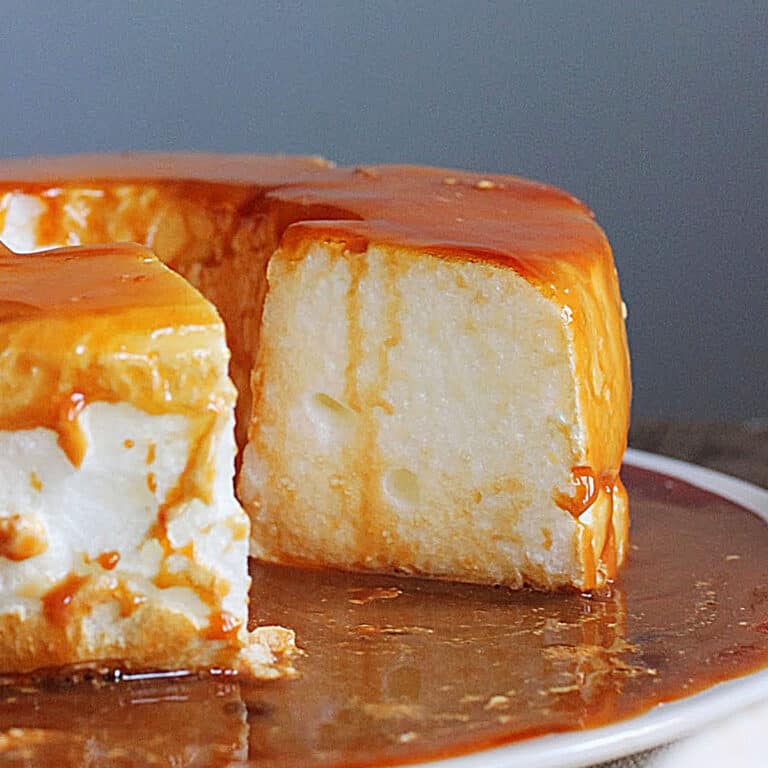 Close up of floating island with a missing slice on a white plate and dulce de leche sauce.