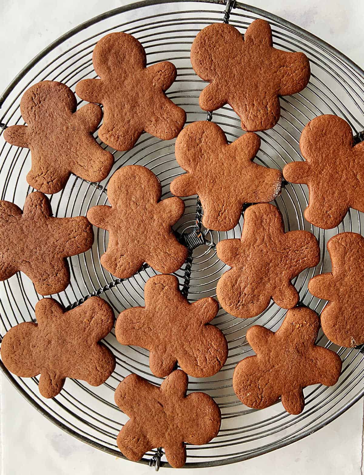 Plain gingerbread people cookies on a round wire rack, white surface.