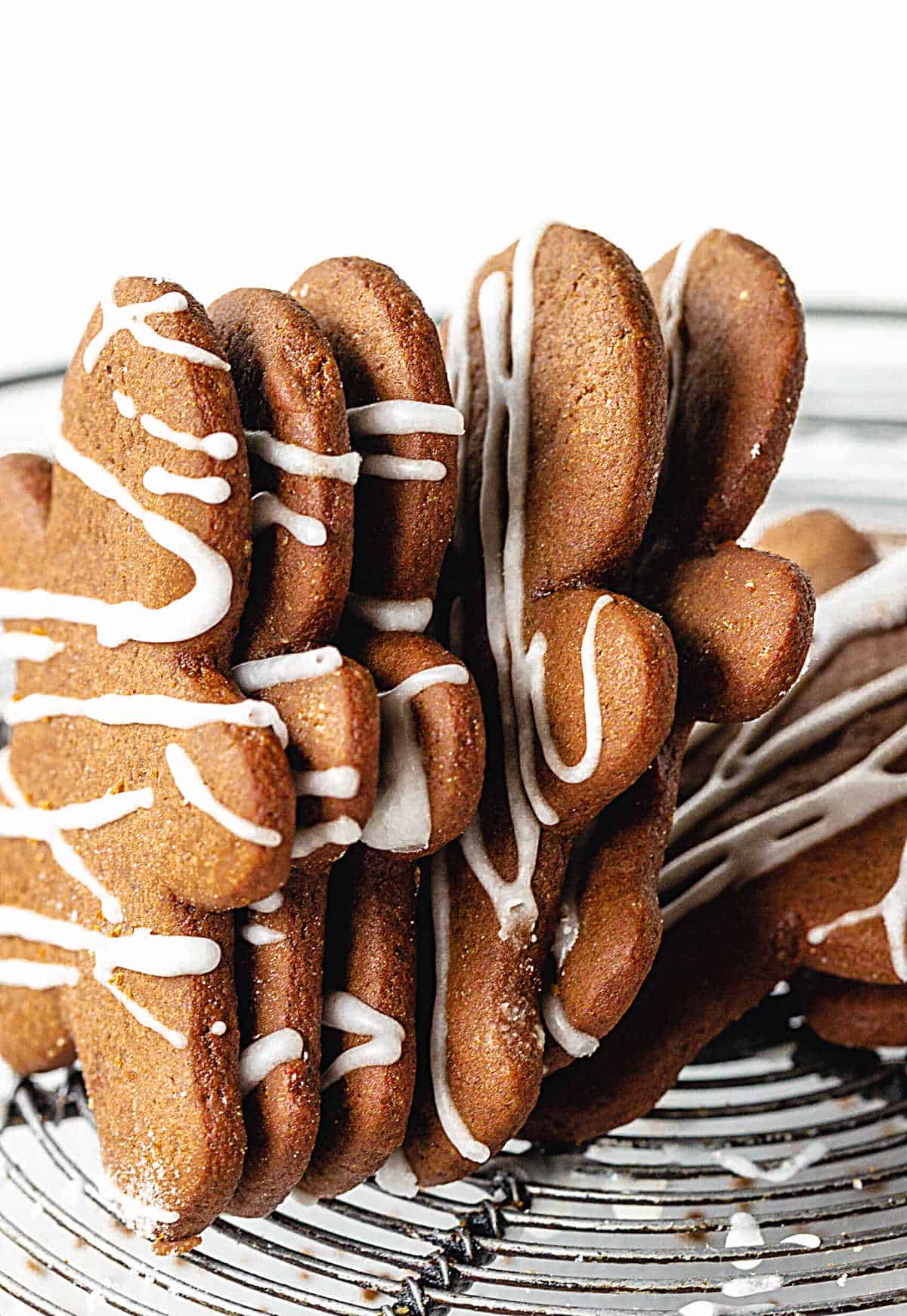 Vertically stacked gingerbread people with icing, on wire rack.