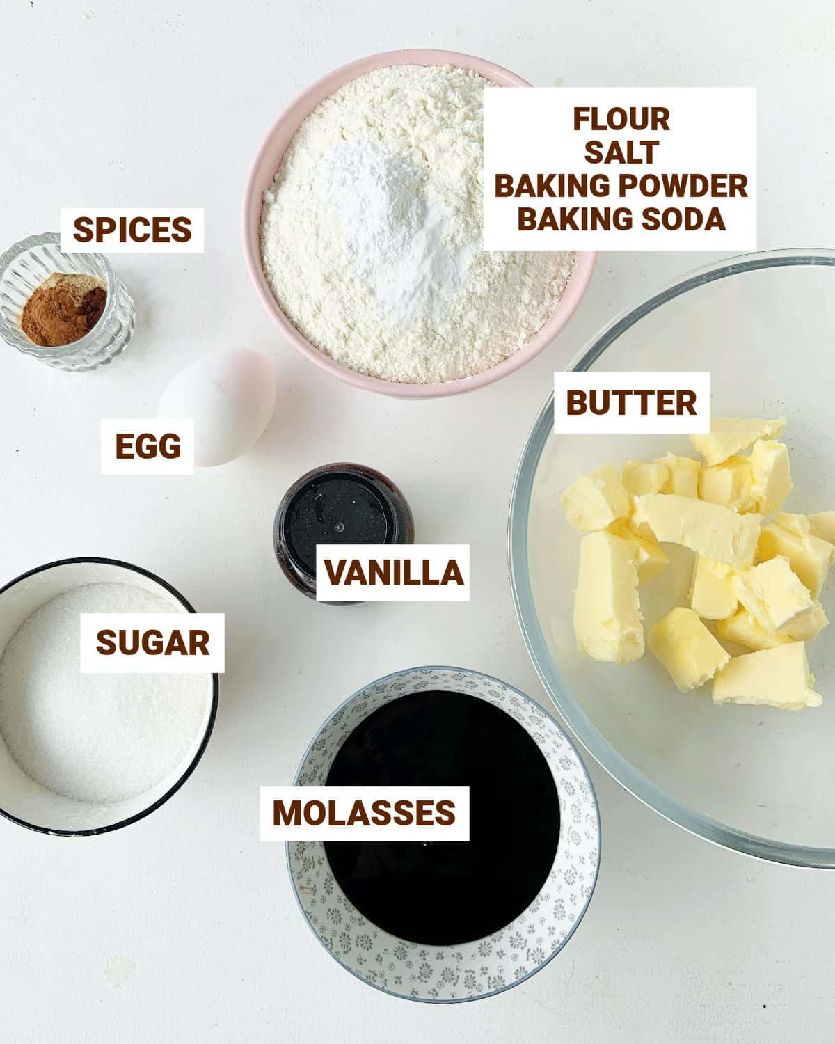 Bowls on white surface with gingerbread cookies ingredients including butter, molasses and spices.