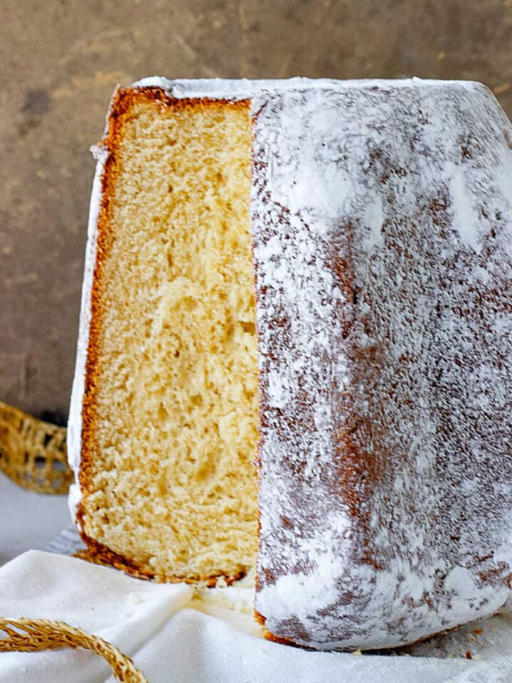 Golden Italian Pandoro bread with powdered sugar and a cut slice on a white cloth with brownish gold background.