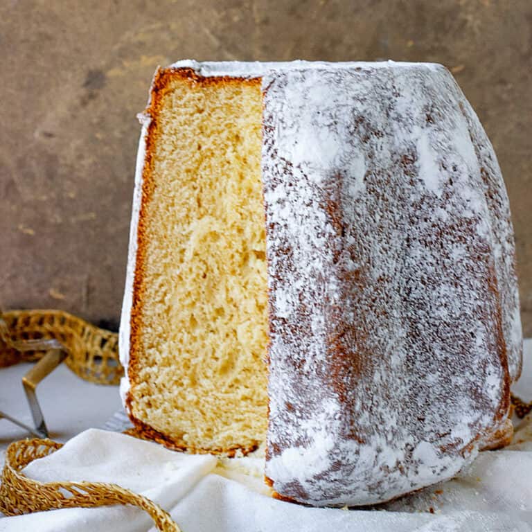 Golden Italian Pandoro bread with powdered sugar and a cut slice on a white cloth with brownish gold background.