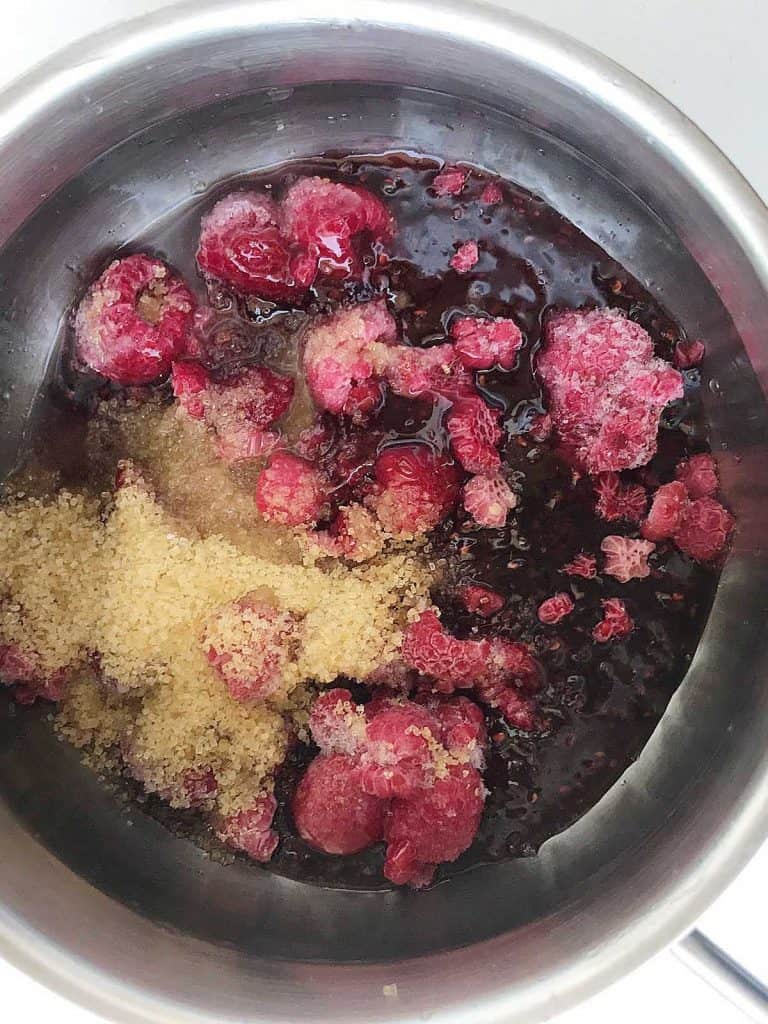 Metal saucepan with raspberries, brown sugar, and lemon juice. View from above.