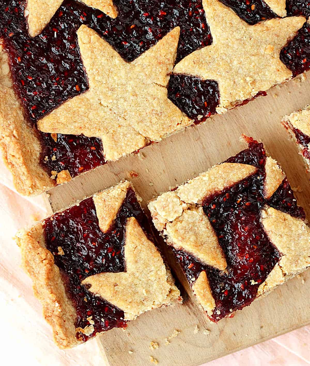 Overview of linzer torte squares with stars on a pink light brown surface.