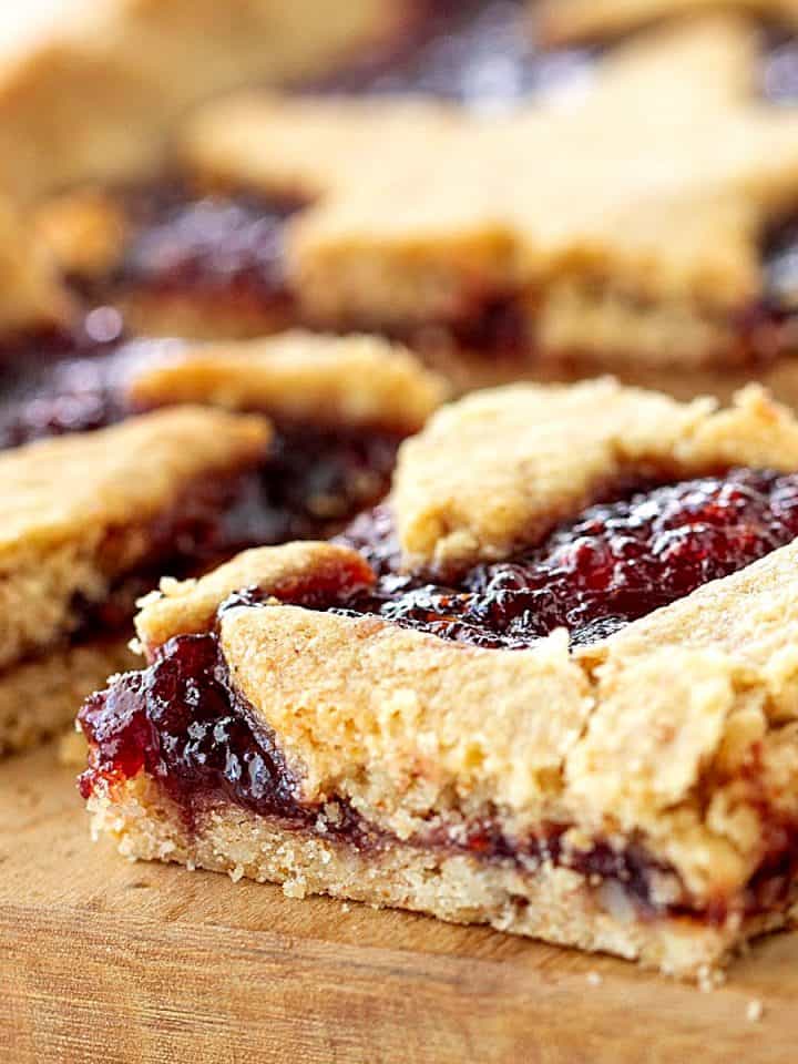 Crumbly squares of raspberry linzer tart on wooden board.