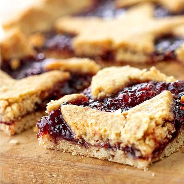 Crumbly squares of raspberry linzer tart on wooden board.