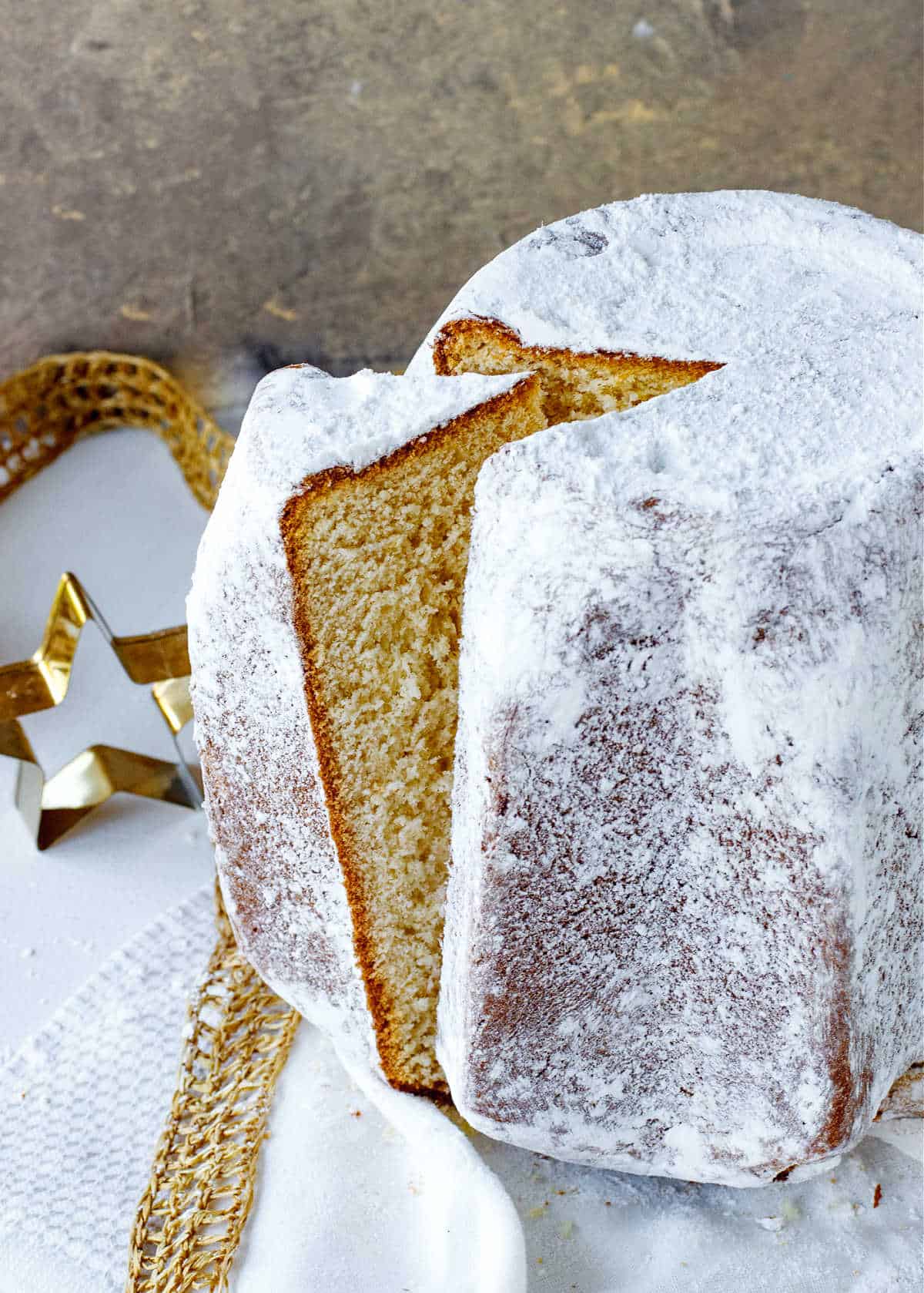 Top view of slice coming out of a whole pandoro bread with powdered sugar; white gold surface and background.