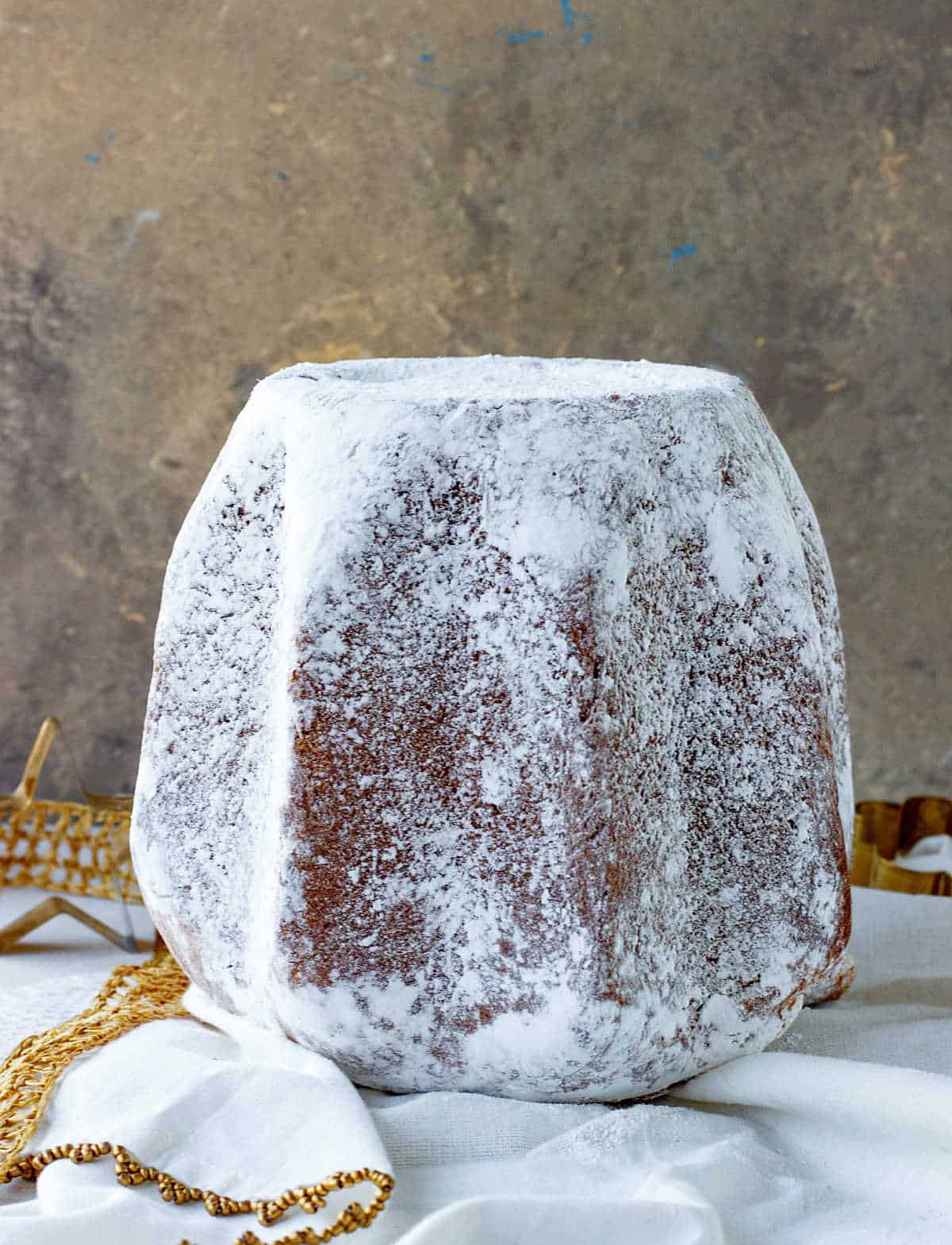 Whole pandoro bread covered in powdered sugar on white golden background