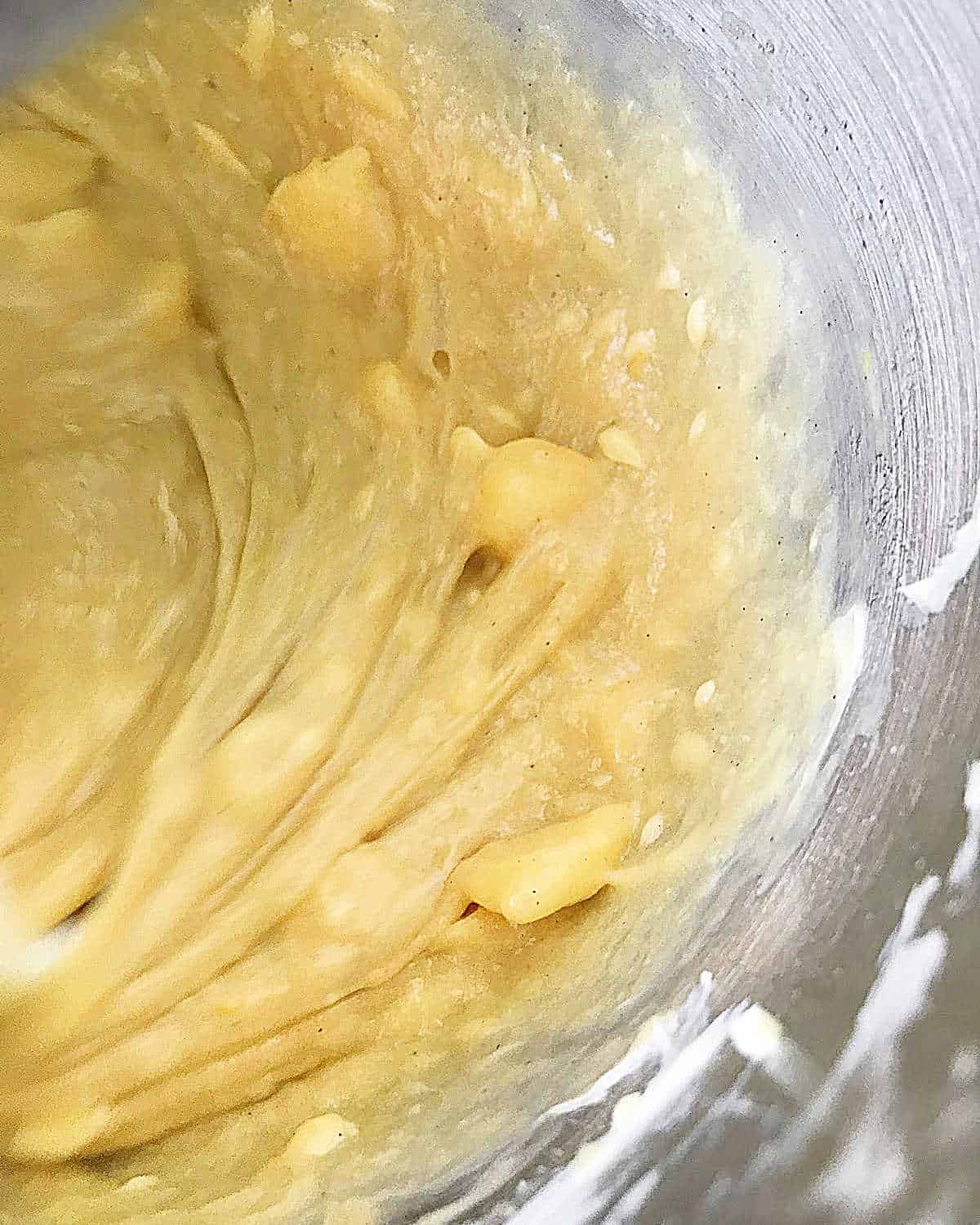 Golden pandoro dough being beaten with butter in a metal bowl. Close up.