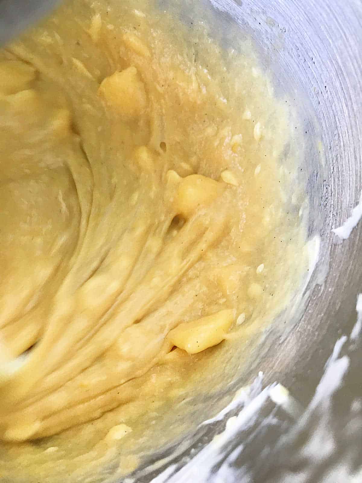 Golden pandoro dough being beaten with butter in a metal bowl
