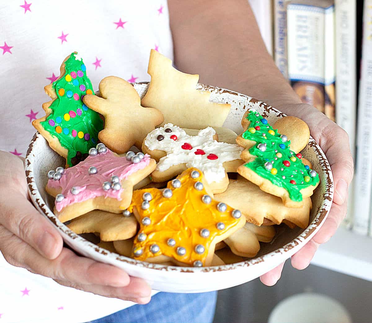 White bowl with frosted sugar cookies held by person with white stars t-shirt.