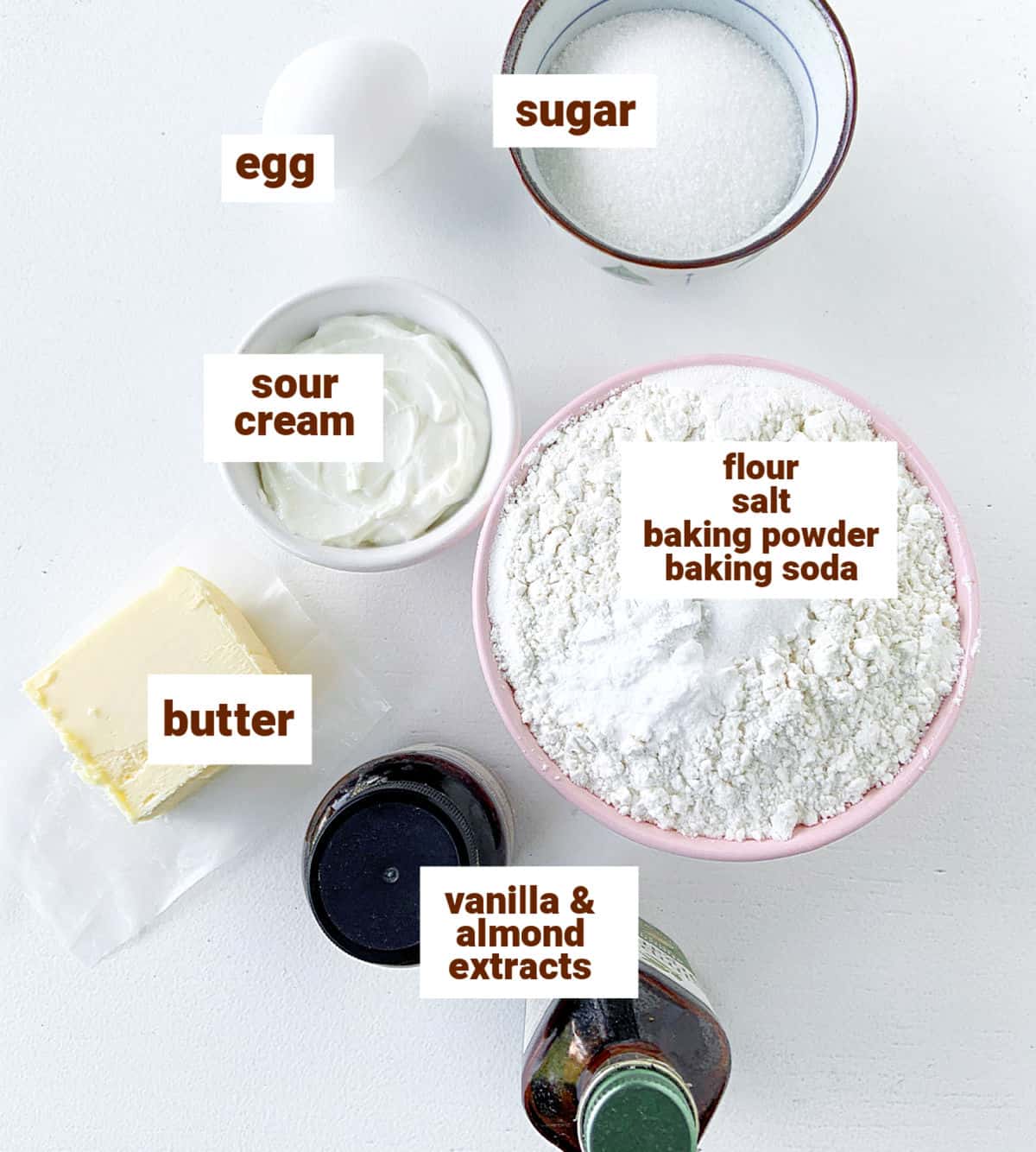 Bowls and bottles of ingredients for sour cream sugar cookies on a white surface