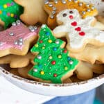 Several frosted colorful holiday cookies on white bowl, red text on image