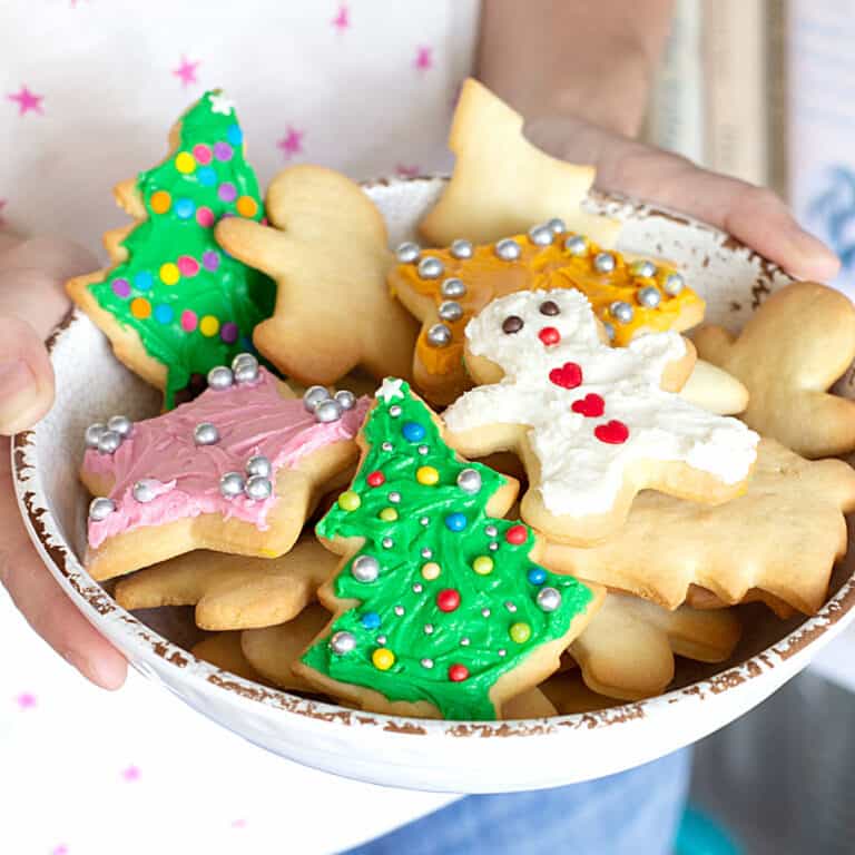 A white shallow bowl with colorful frosted holiday cutout cookies being held in the air.