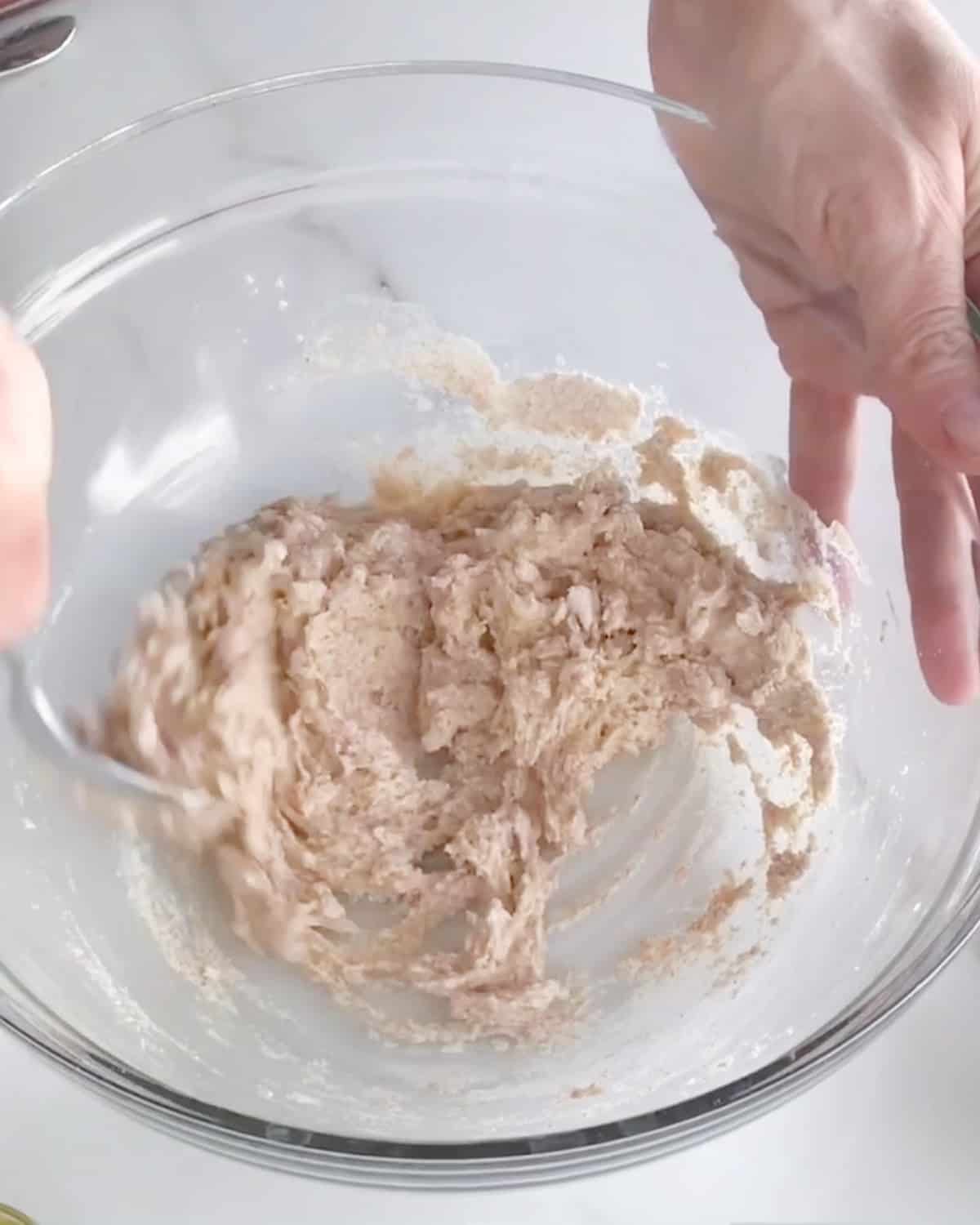 Mixing a whole wheat bread sponge in a glass bowl on a white marble surface.