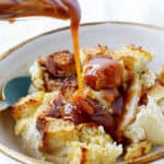 Pouring dulce de leche on serving of apple bread pudding, white bowl and background