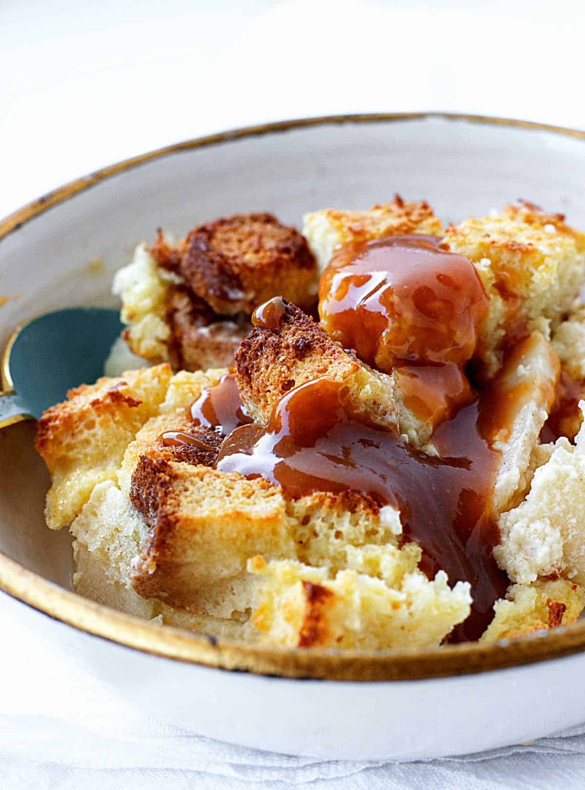 Serving of apple bread pudding in a white gold-rimmed bowl, caramel topping and white background