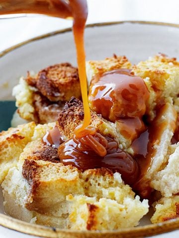 Close up of caramel being poured on a white bowl with apple bread pudding.