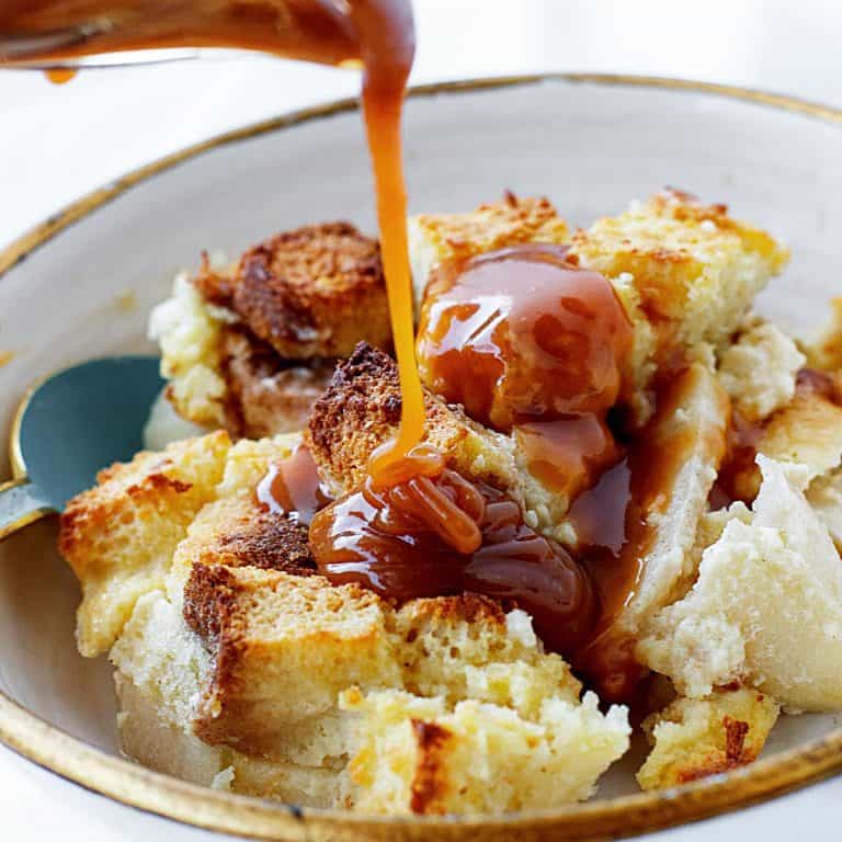 Close up of caramel being poured on a white bowl with apple bread pudding.