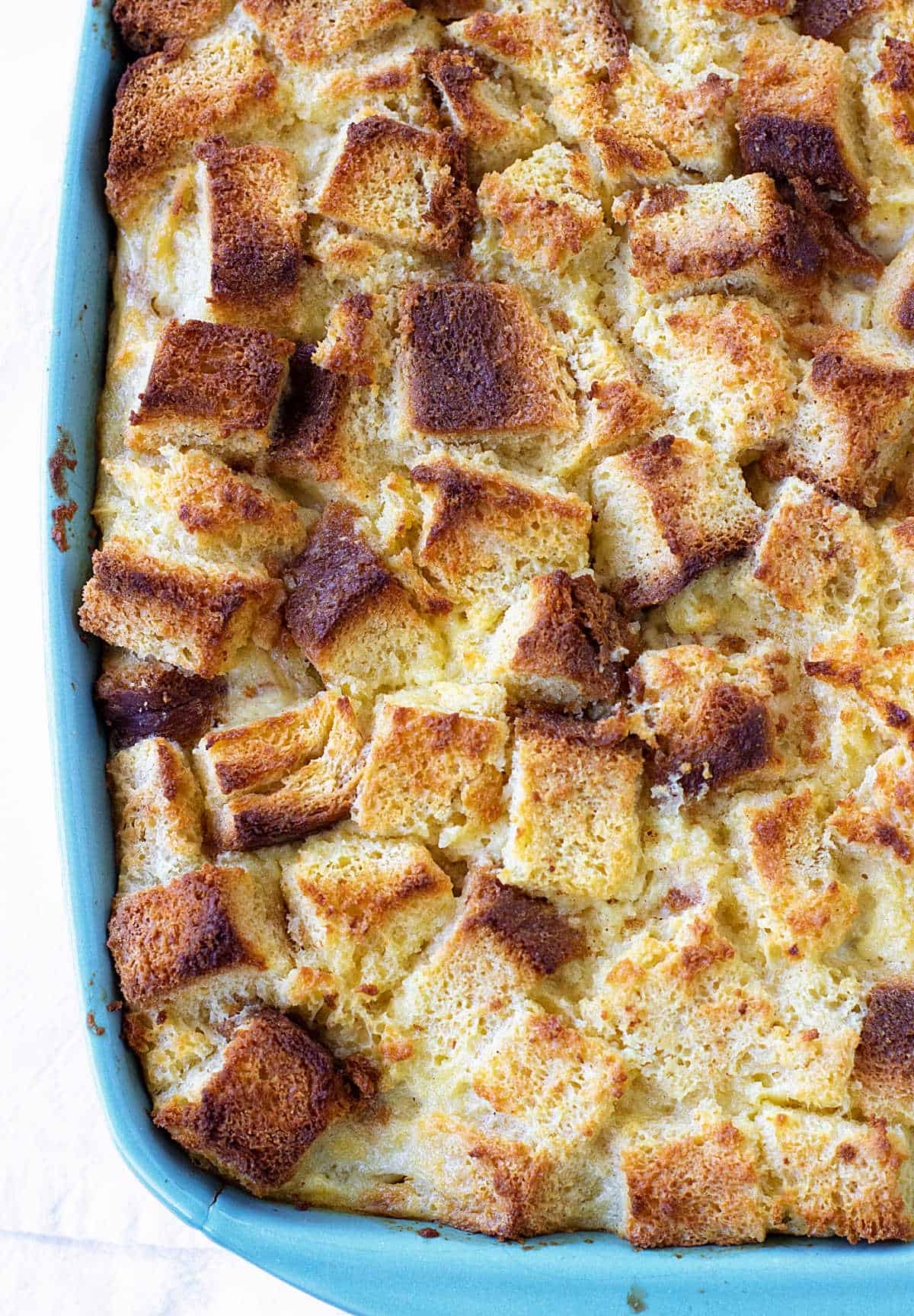 Partial top view of bread pudding in blue dish on white surface.