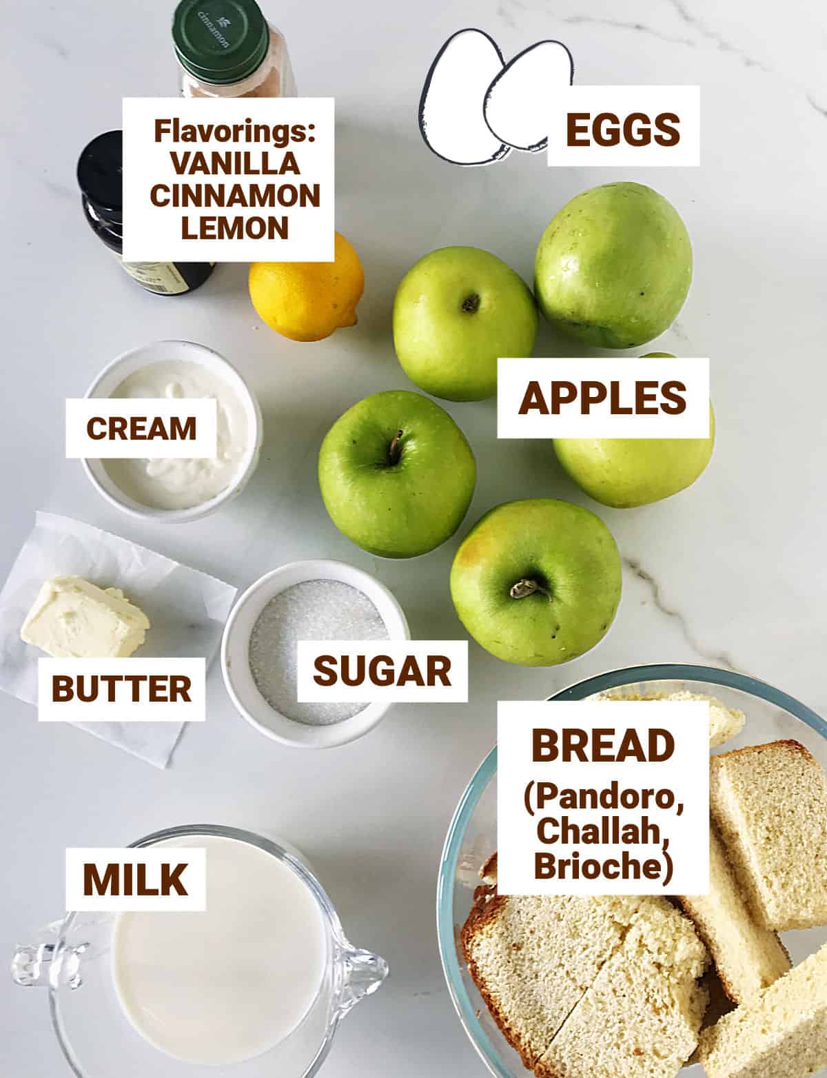 Ingredients for apple bread pudding in bowls and on white surface, including eggs and small bottles.