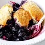 White bowl with serving of blueberry cobbler, a spoon