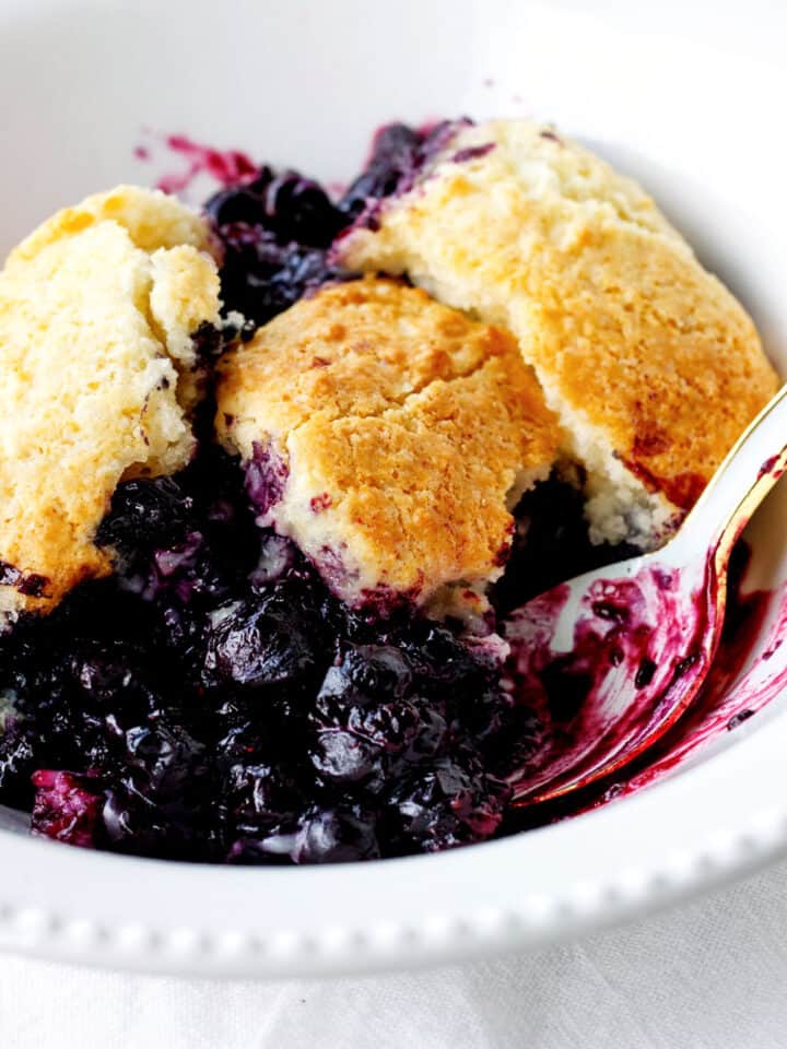 White bowl with serving of blueberry cobbler, a spoon