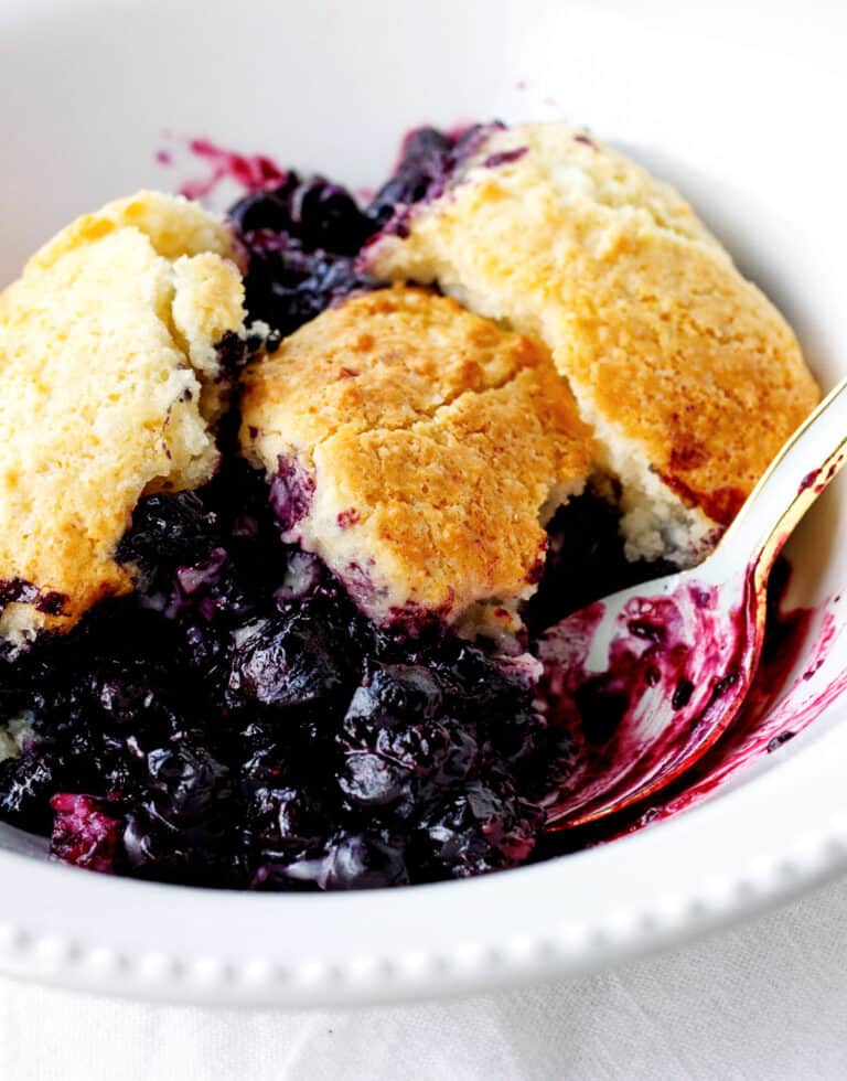 White bowl with serving of blueberry cobbler, a spoon