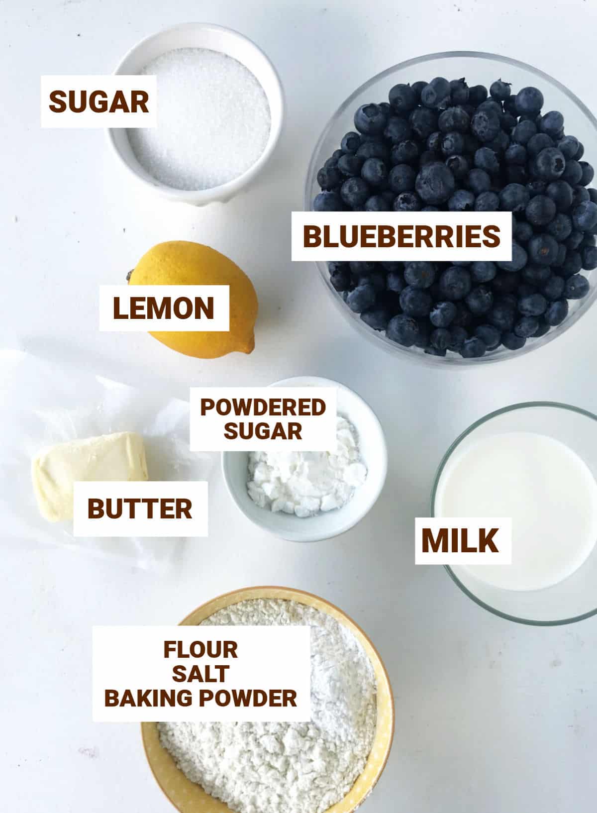 Bowls with ingredients for blueberry lemon cobbler on a white surface