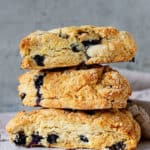 Three blueberry scones stacked on a white surface with grey background