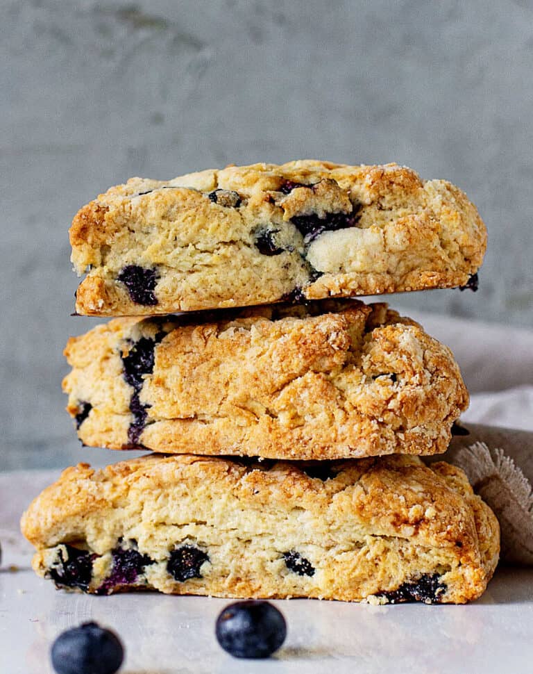 Three blueberry scones stacked on a white surface with grey background