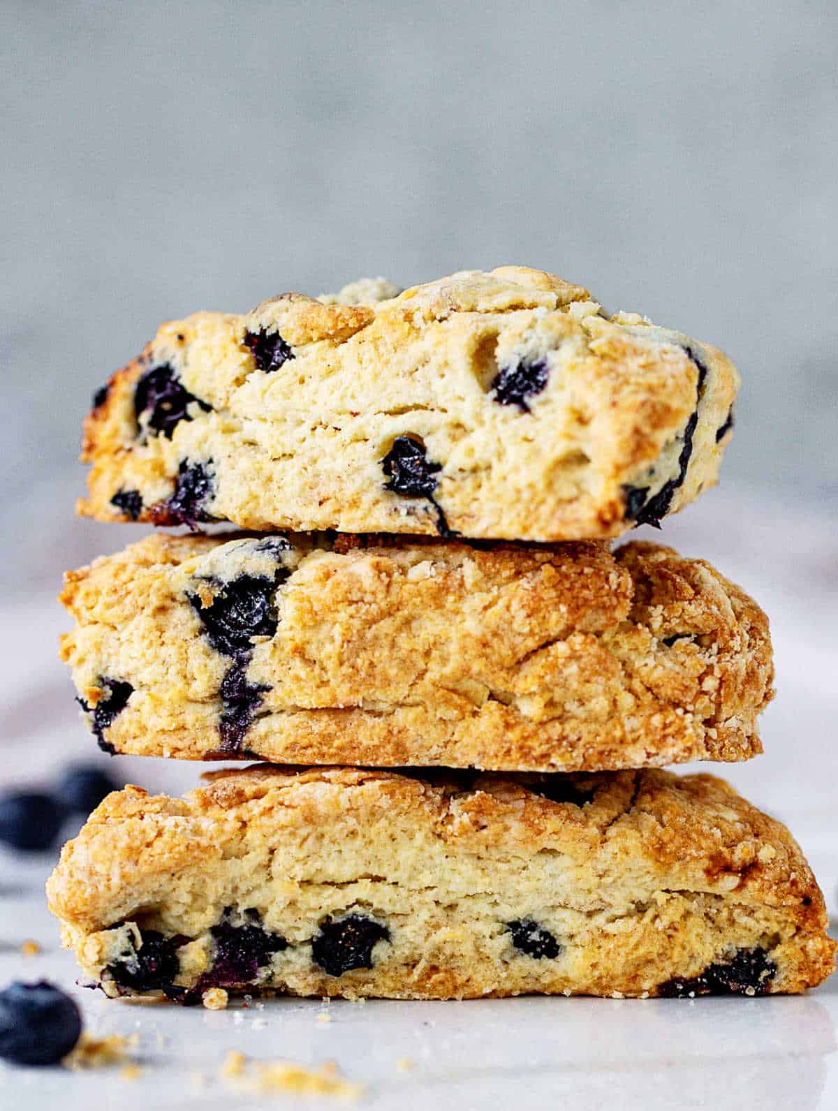 Stack of three blueberry scones on white surface and grey background