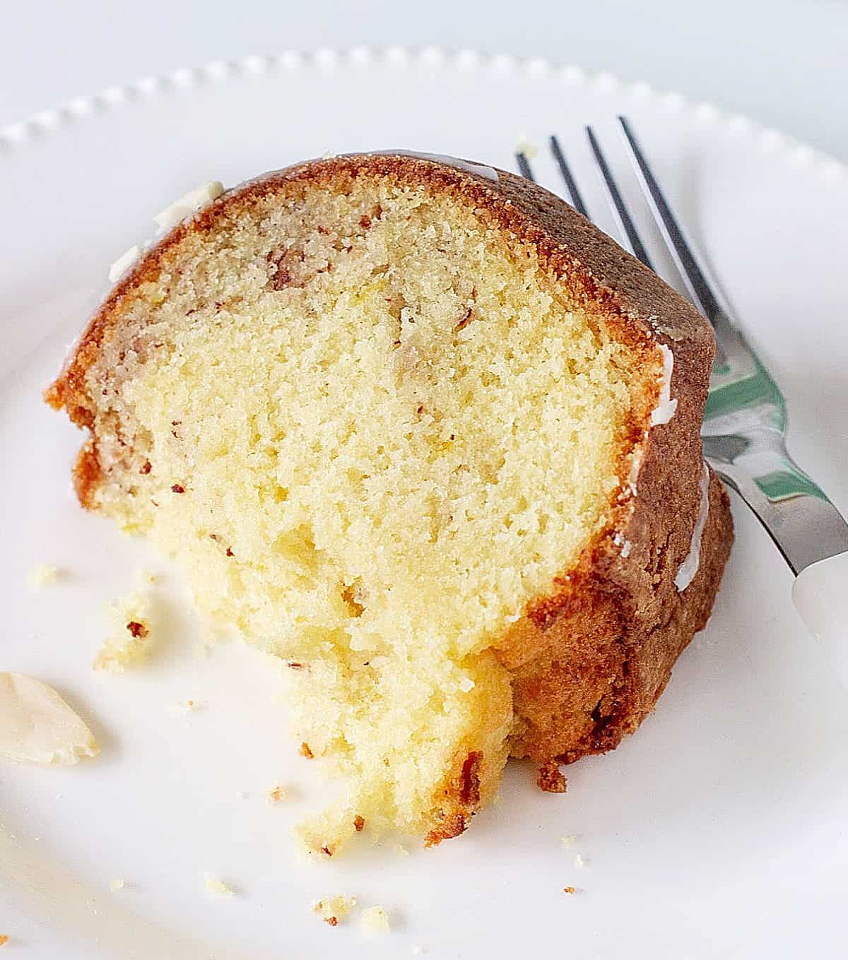 Close up of bitten slice of lemon bundt cake on white plate