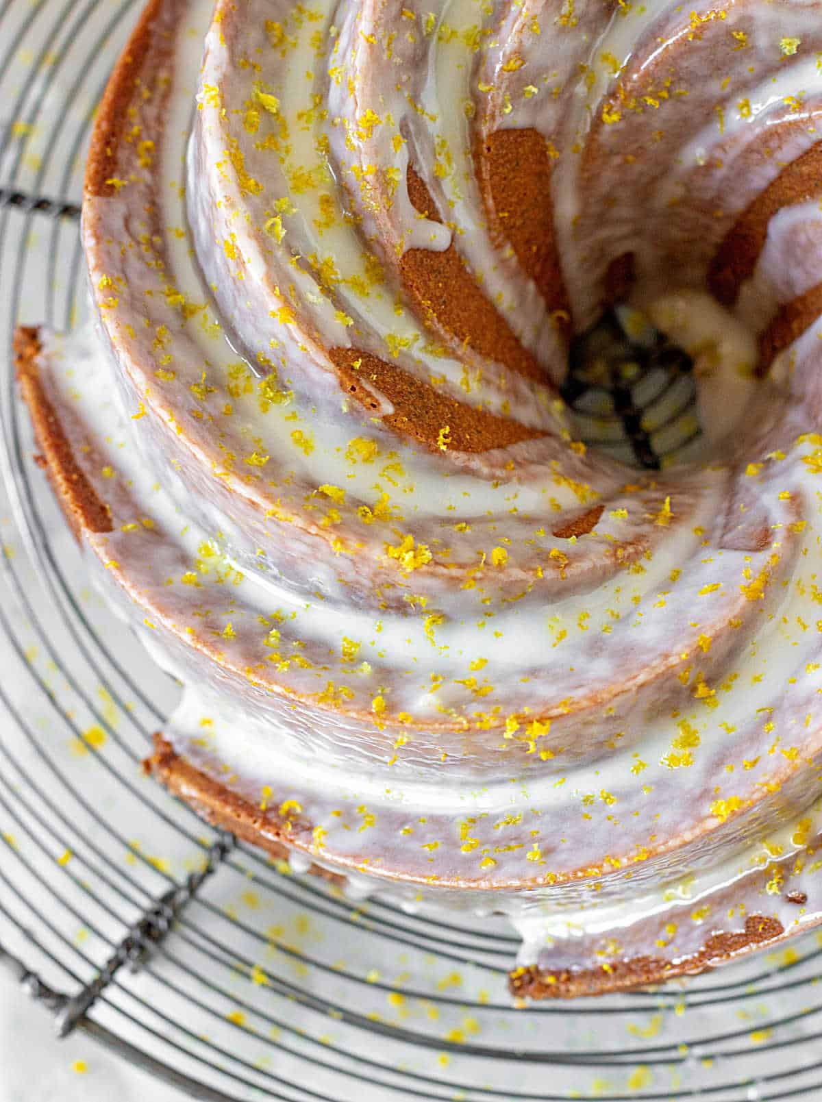 Top view of partial glazed bundt cake with lemon zest on a wire rack.