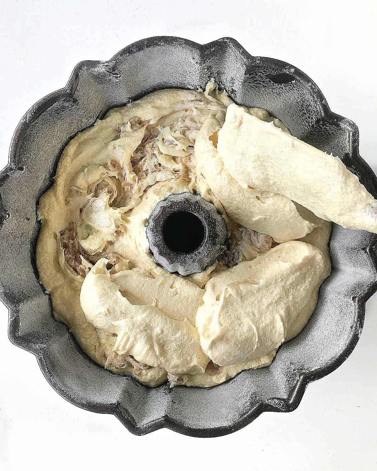 Adding cake batter to layer of swirled batter. Bundt cake. White surface.