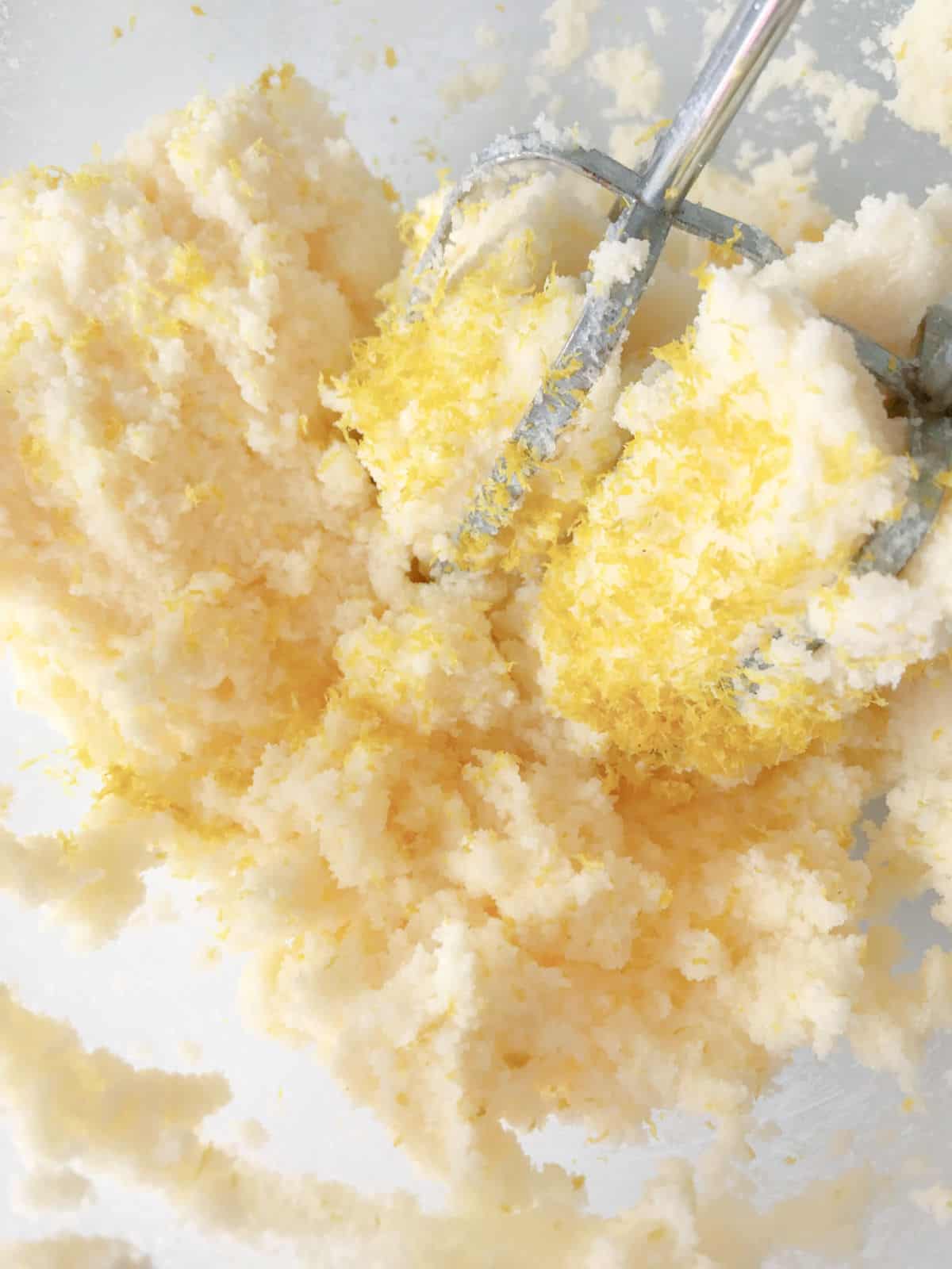 Lemon zest added to butter cake batter in bowl with metal beaters. Close up image.